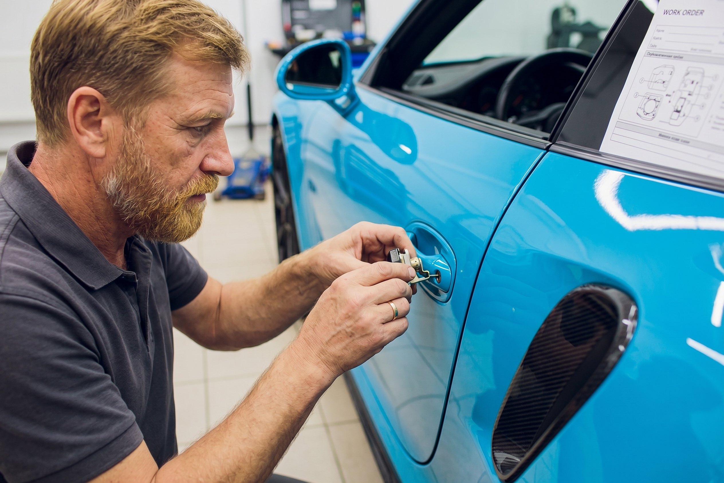 A technician working the door lock of a car with a hand tool